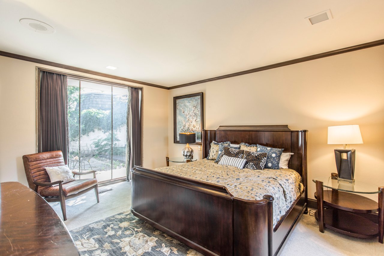 Furnished bedroom with a dark wood bed, patterned bedding, and sliding glass doors to a garden.