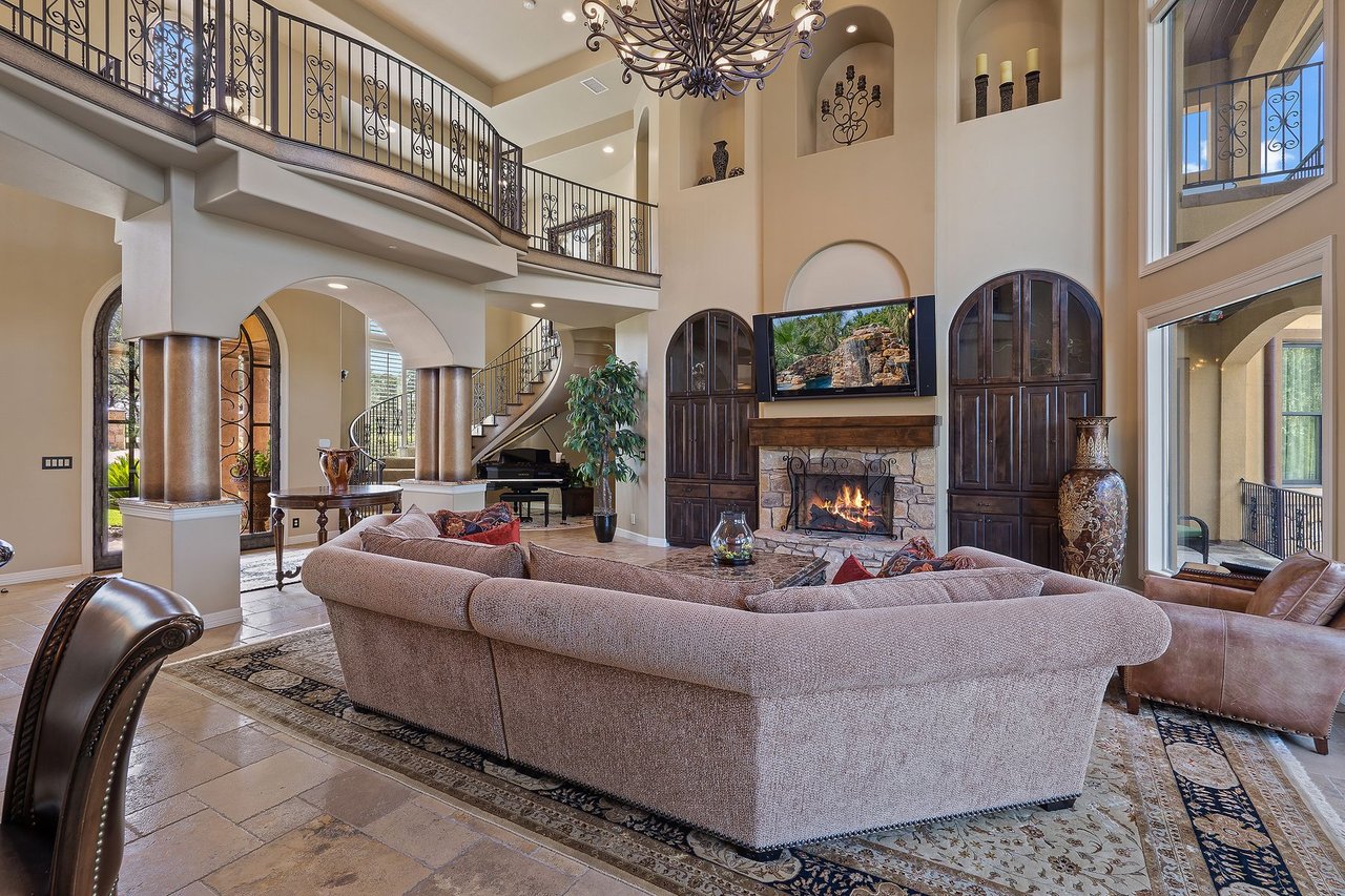 Great room with a stone fireplace, built-in wood cabinetry, and a view to the curved staircase at 25715 Cliff Circle, Lakecliff on Lake Travis, Spicewood, Texas.