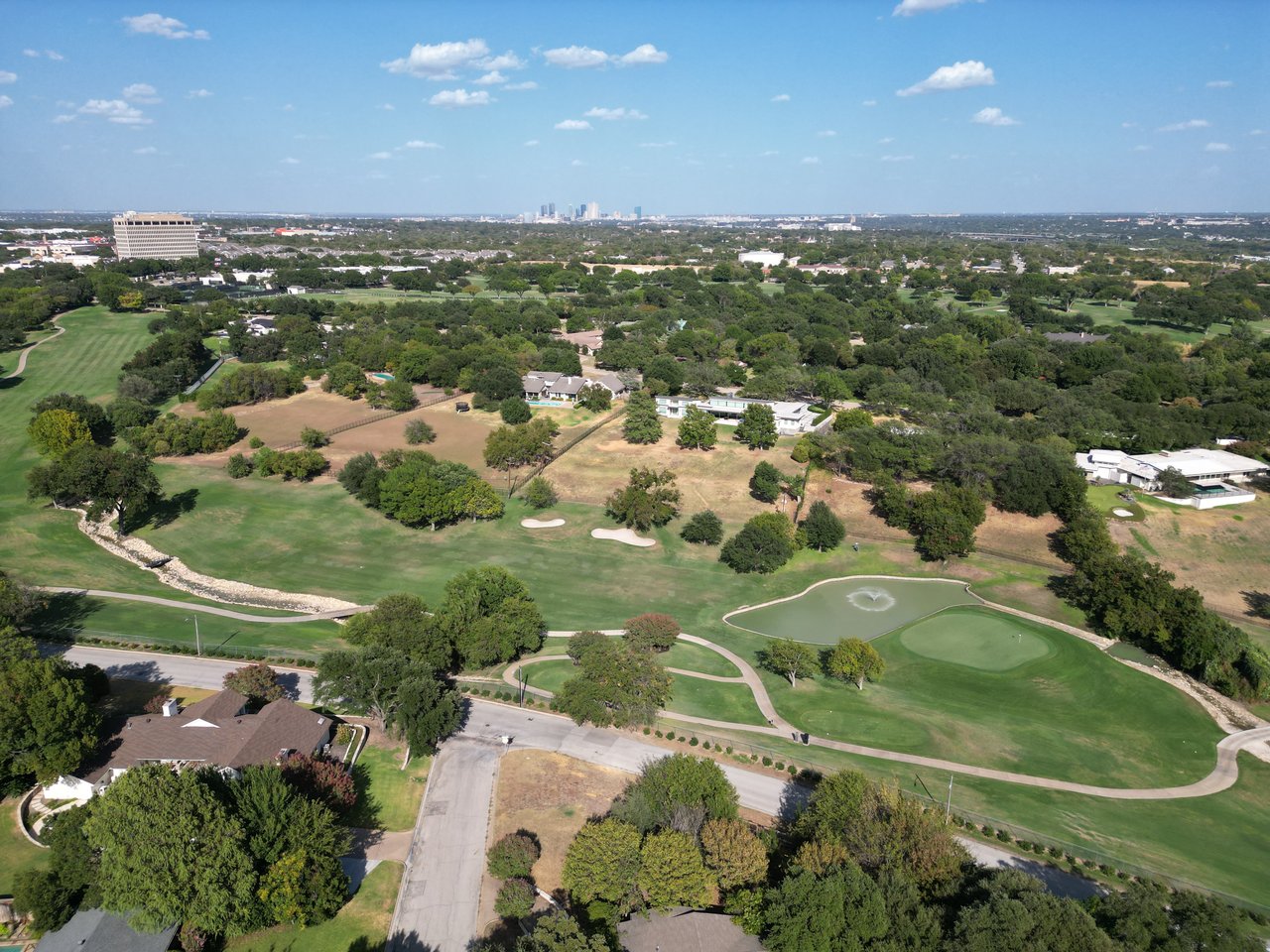 Aerial view of Ridglea golf course with a pond, tree-lined greens, and the distant city skyline.