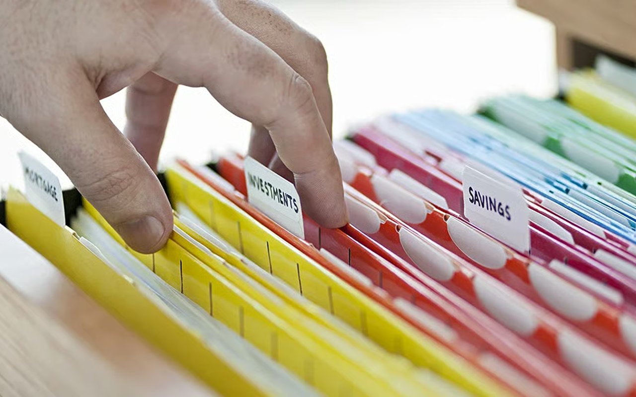 A hand sorts color-coded financial folders labeled Investments and Savings.