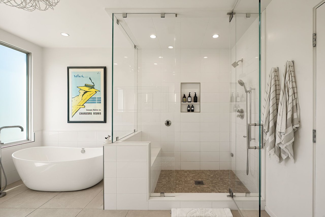 Bright bathroom with a freestanding tub and glass shower featuring a tiled niche and mosaic floor.