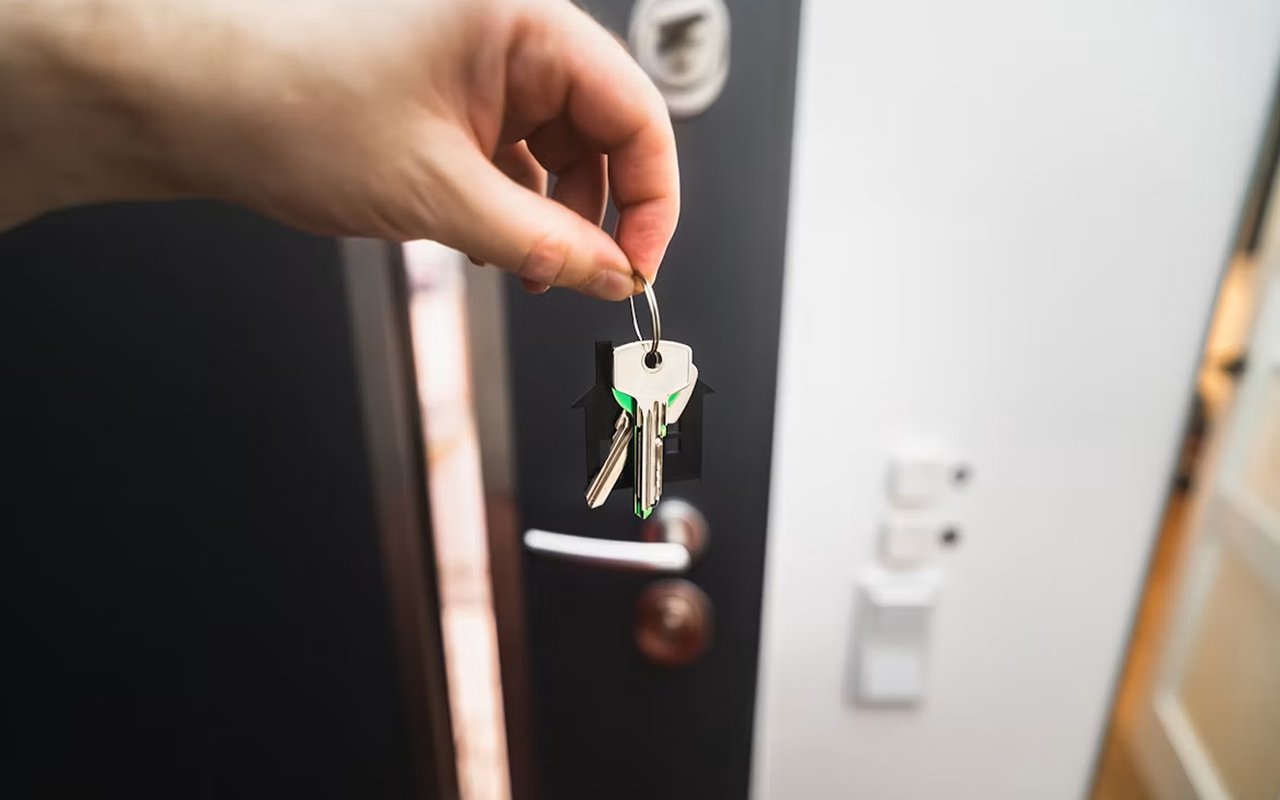 A hand holds keys in front of an open door.