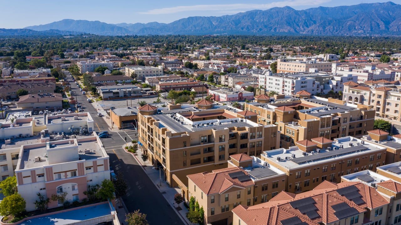 Aerial view of a dense neighborhood with red-tile roofs and mountains in the distance.