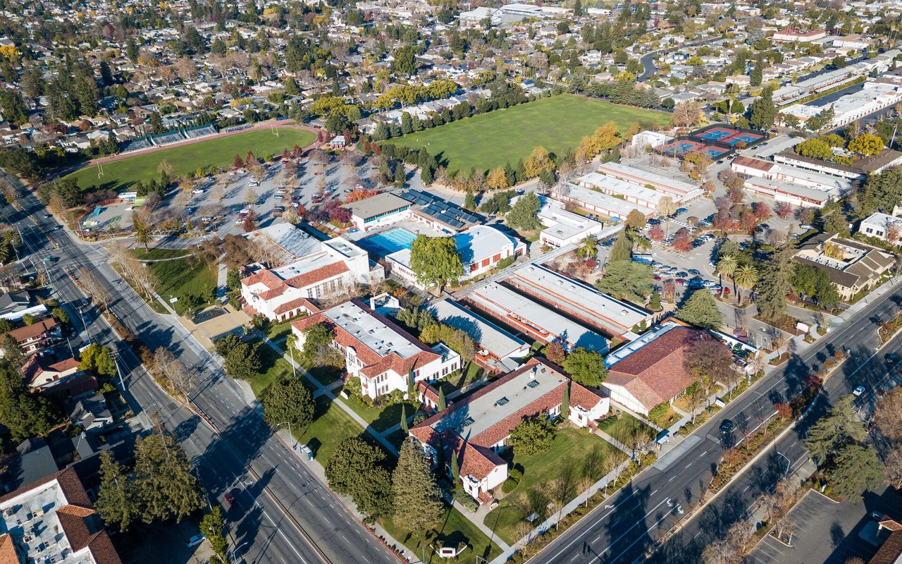 Aerial neighborhood view with a large green field, sports courts, and low-rise buildings.
