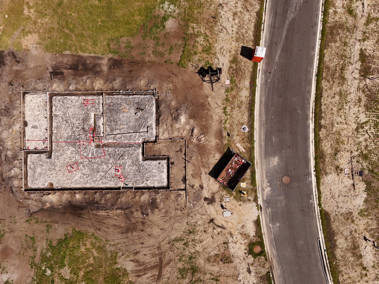 Aerial view of a home foundation under construction beside a paved road.