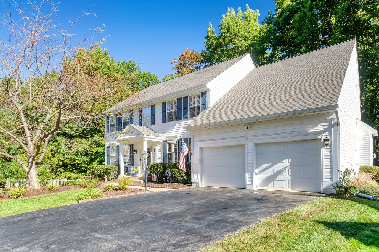 White two-story house with blue shutters, a covered entry, and a two-car garage.