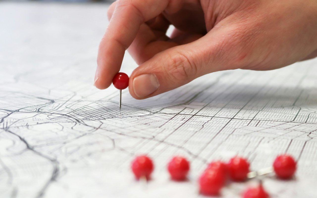 A hand places a red pushpin on a printed street map.