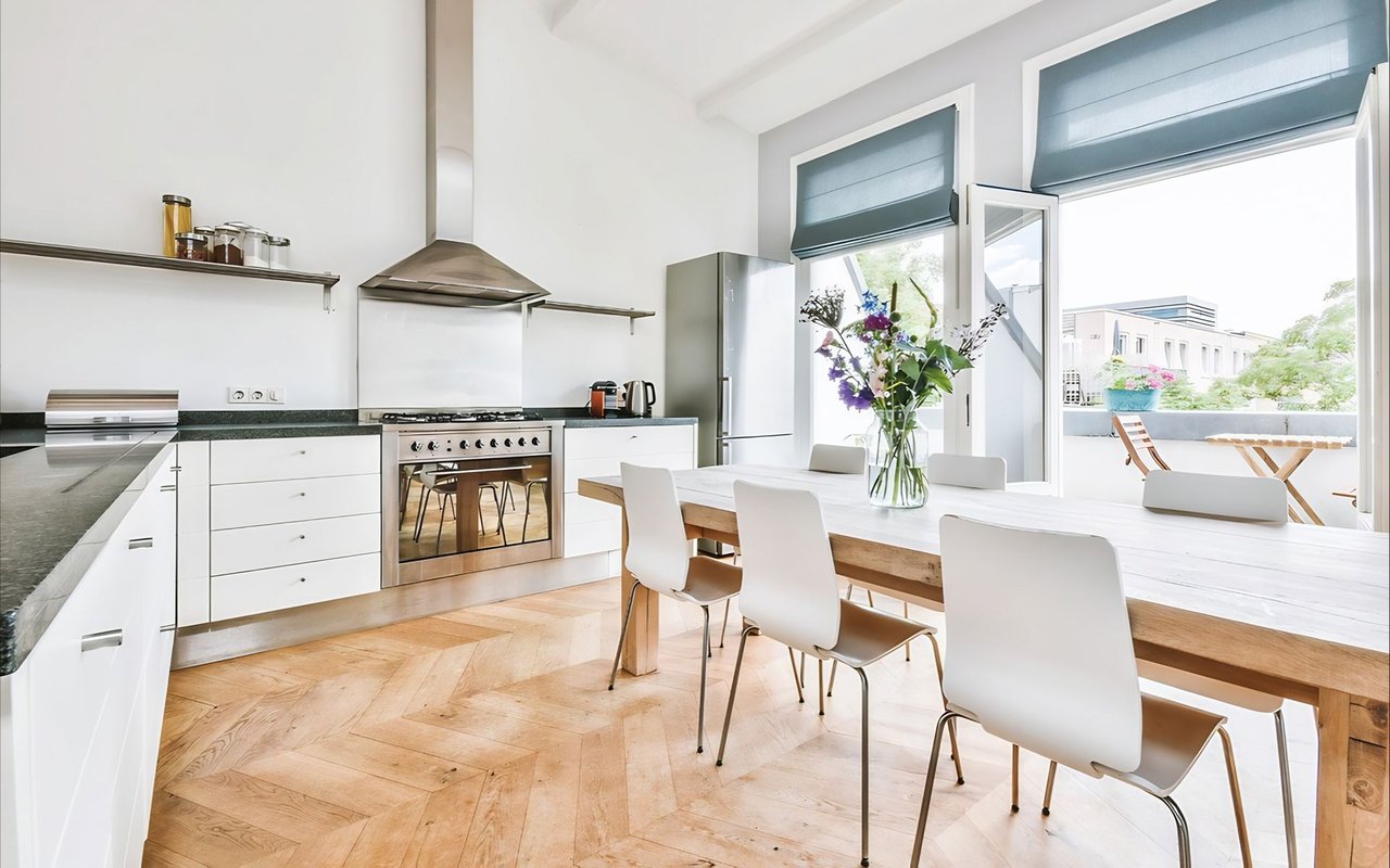 Modern kitchen and dining area with white cabinetry, a long wooden table, and an open door to the terrace.