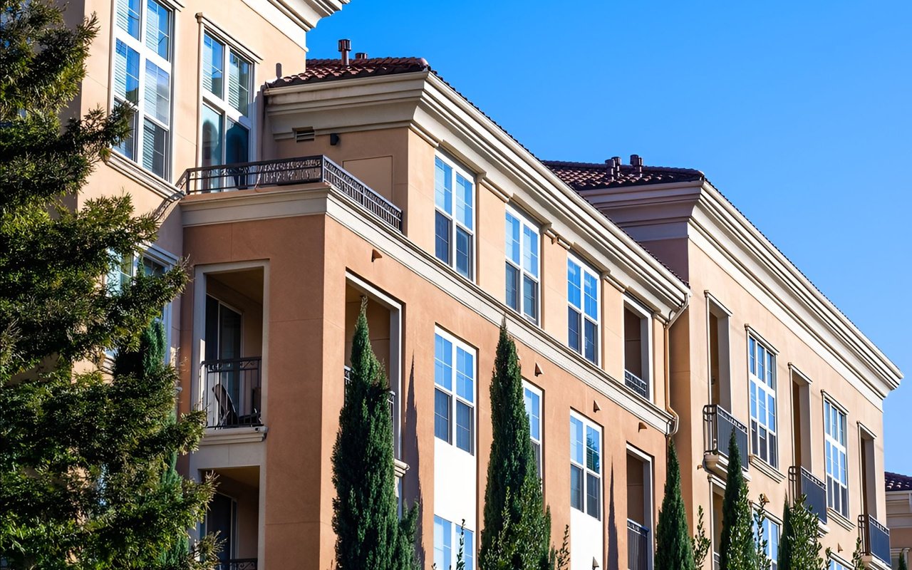 Multistory peach-stucco condominium with balconies, white-trimmed windows, and red tile roofs.