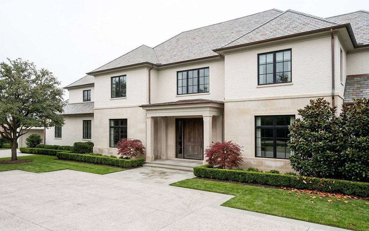 Two-story white brick house with a pale stone facade, covered entrance, and landscaped front lawn.