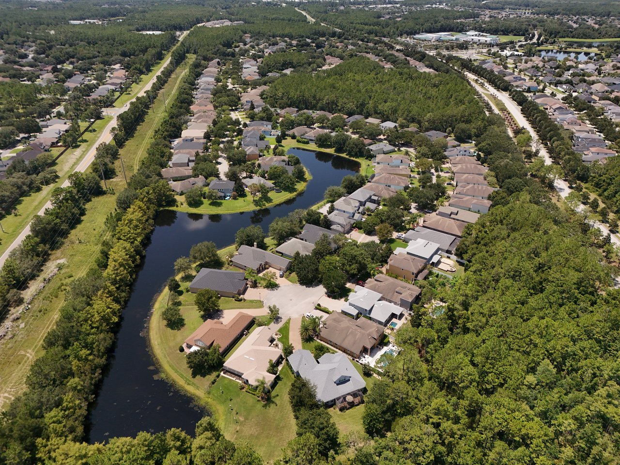 Aerial view of homes surrounding a winding pond, with wooded areas and tree-lined streets.