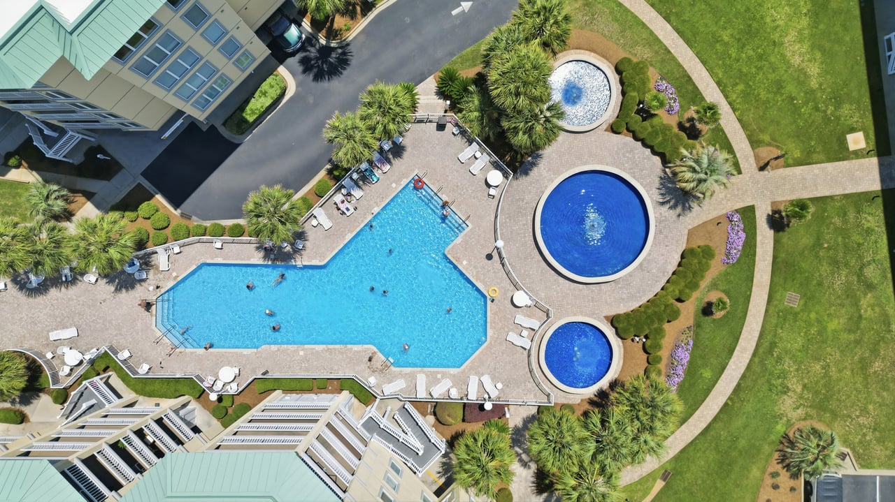 Aerial view of a community pool with two circular pools, palm trees, and surrounding residential buildings.