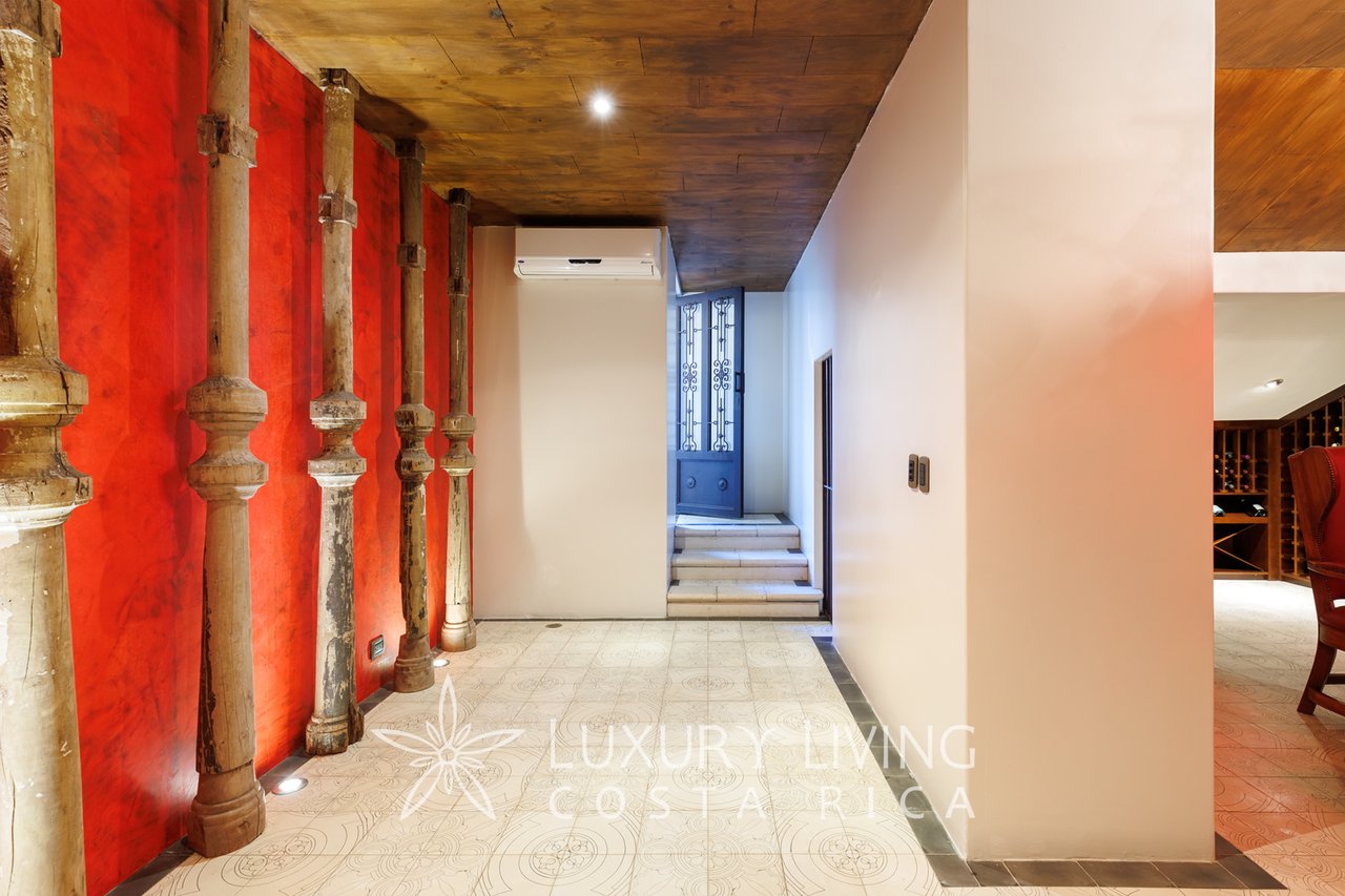 Entry hall with red wall, carved columns, patterned tile, and steps to an ornate door.