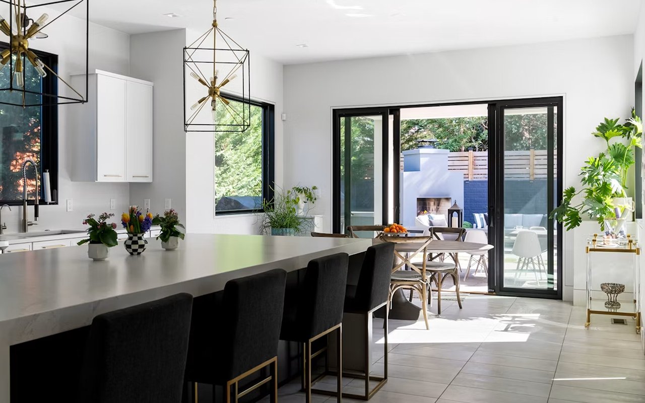 Modern kitchen with a long island, black stools, and sliding doors to a patio.