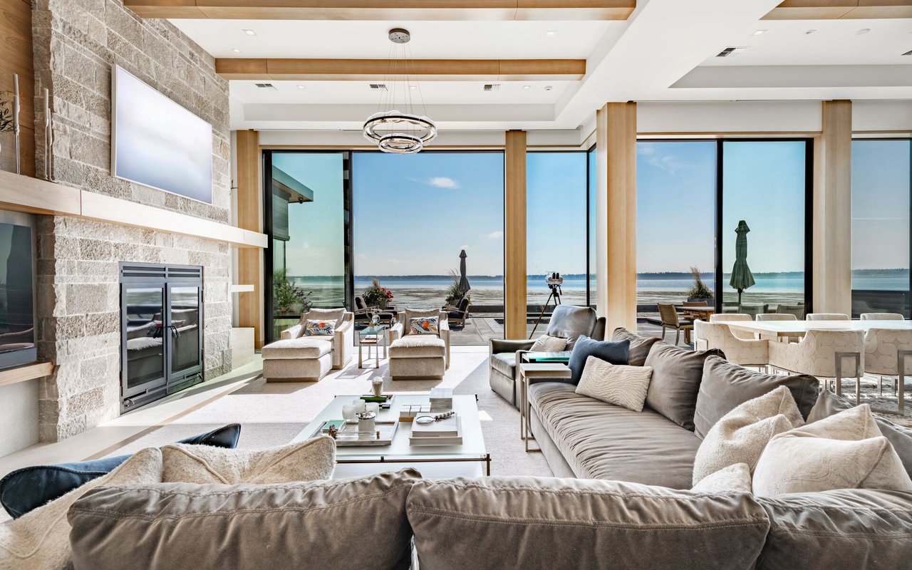 Living room with a stone fireplace and expansive windows overlooking the water.