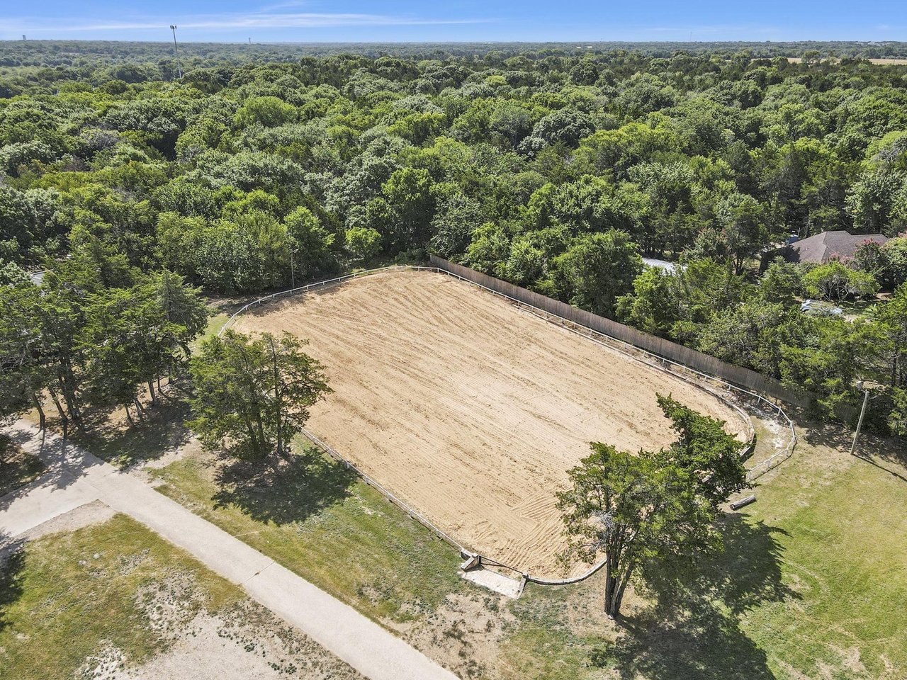 Fenced dirt field surrounded by trees, viewed from above.