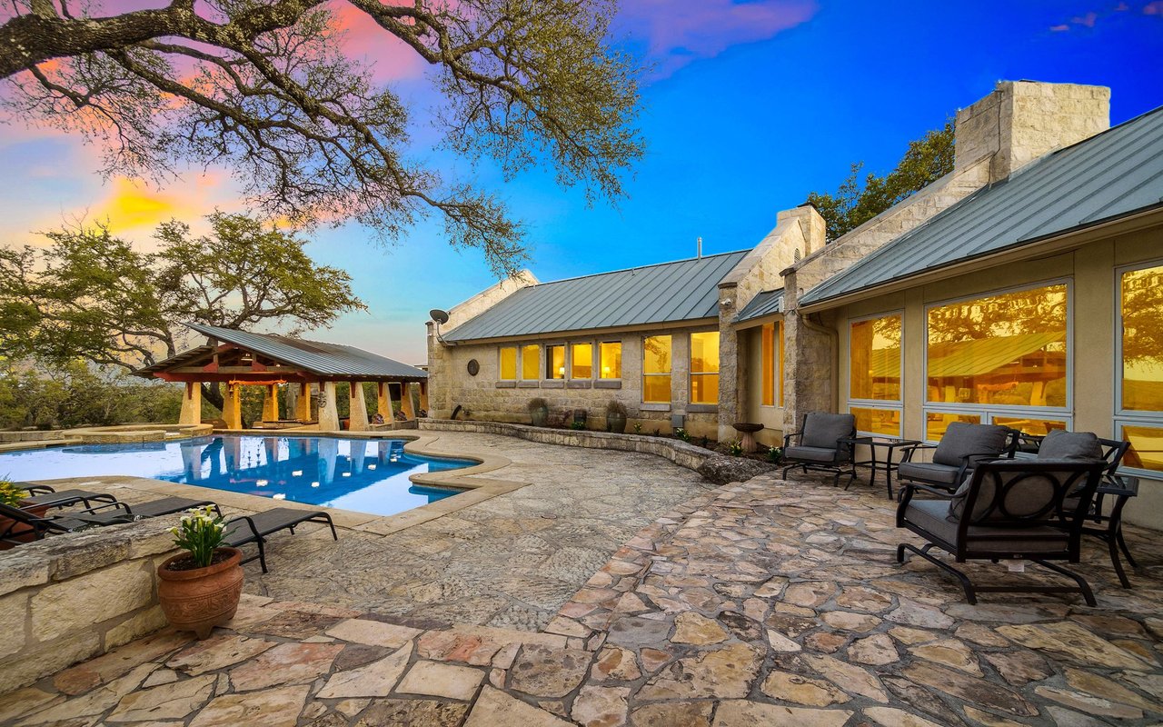 Stone home with a swimming pool, covered patio, and stone terrace at sunset.