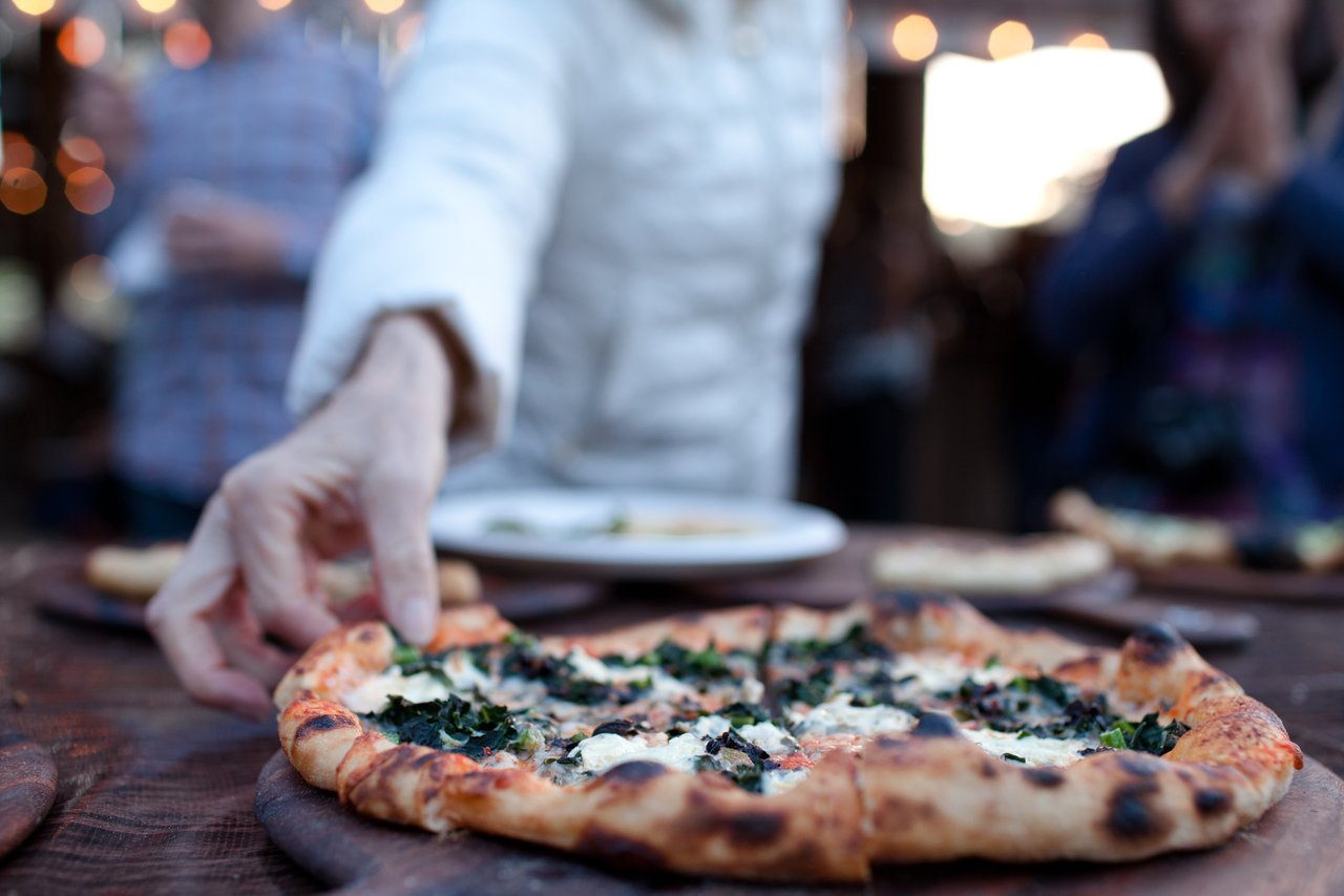 Wood-fired pizza topped with leafy greens and cheese on a wooden table.