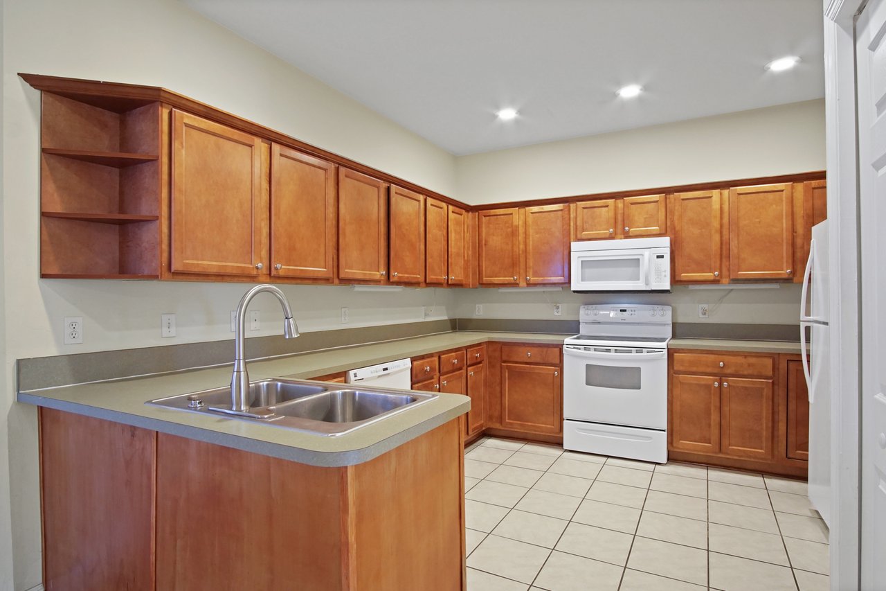 Kitchen at 5441 Hampton Hill Circle, Tallahassee, Florida 32311 with wood cabinets, white appliances, double sink, and tile floors.