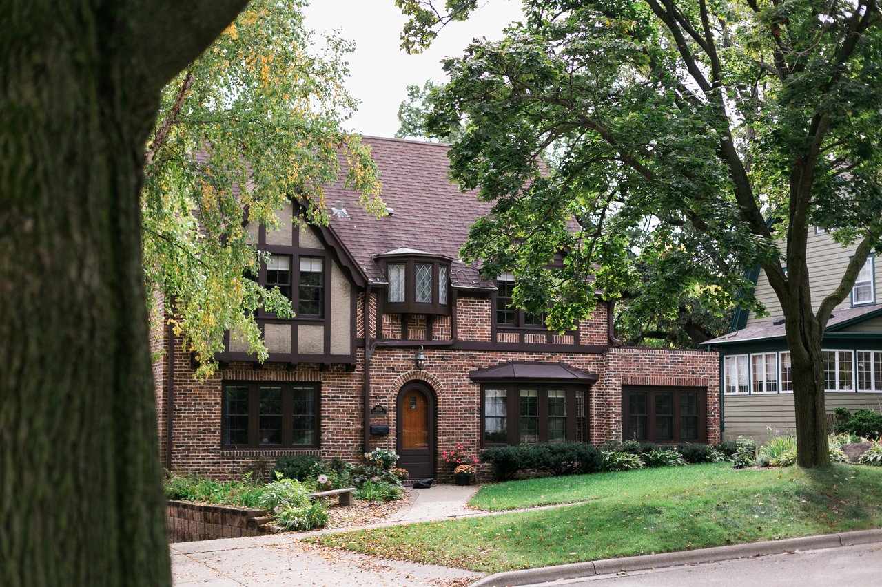 A beautiful, historic Tudor-style brick home featuring dark wood half-timbering, a classic arched doorway, and mature landscaping in the prestigious Near West Side of Madison. This architectural style represents the highly sought-after, premium real estate found in established neighborhoods like Nakoma and University Heights.