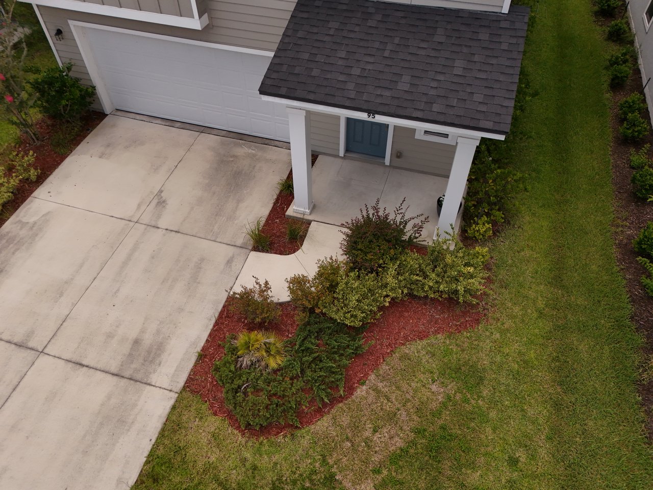 Aerial view of a home’s front entry, garage, driveway, and landscaped lawn.