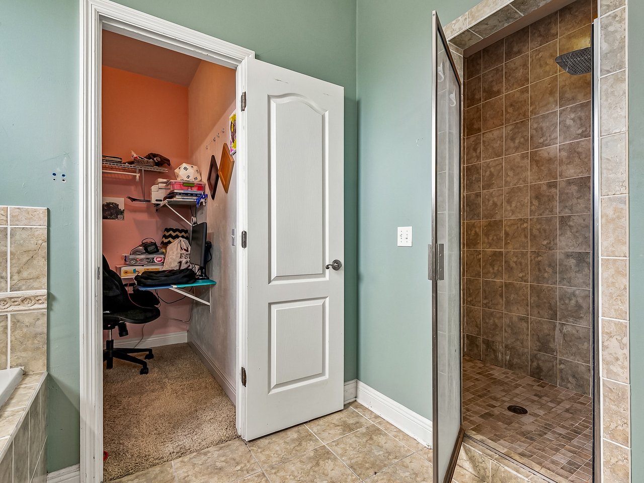 Bathroom with a brown-tiled walk-in shower and an open door to a small office nook.