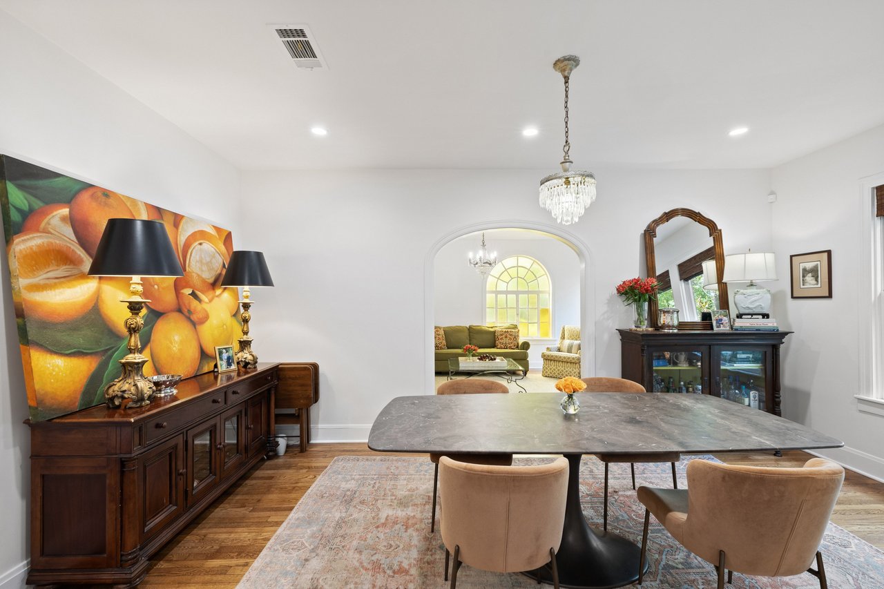 Dining room with a stone-top table, upholstered chairs, and an arched opening to a sitting room.