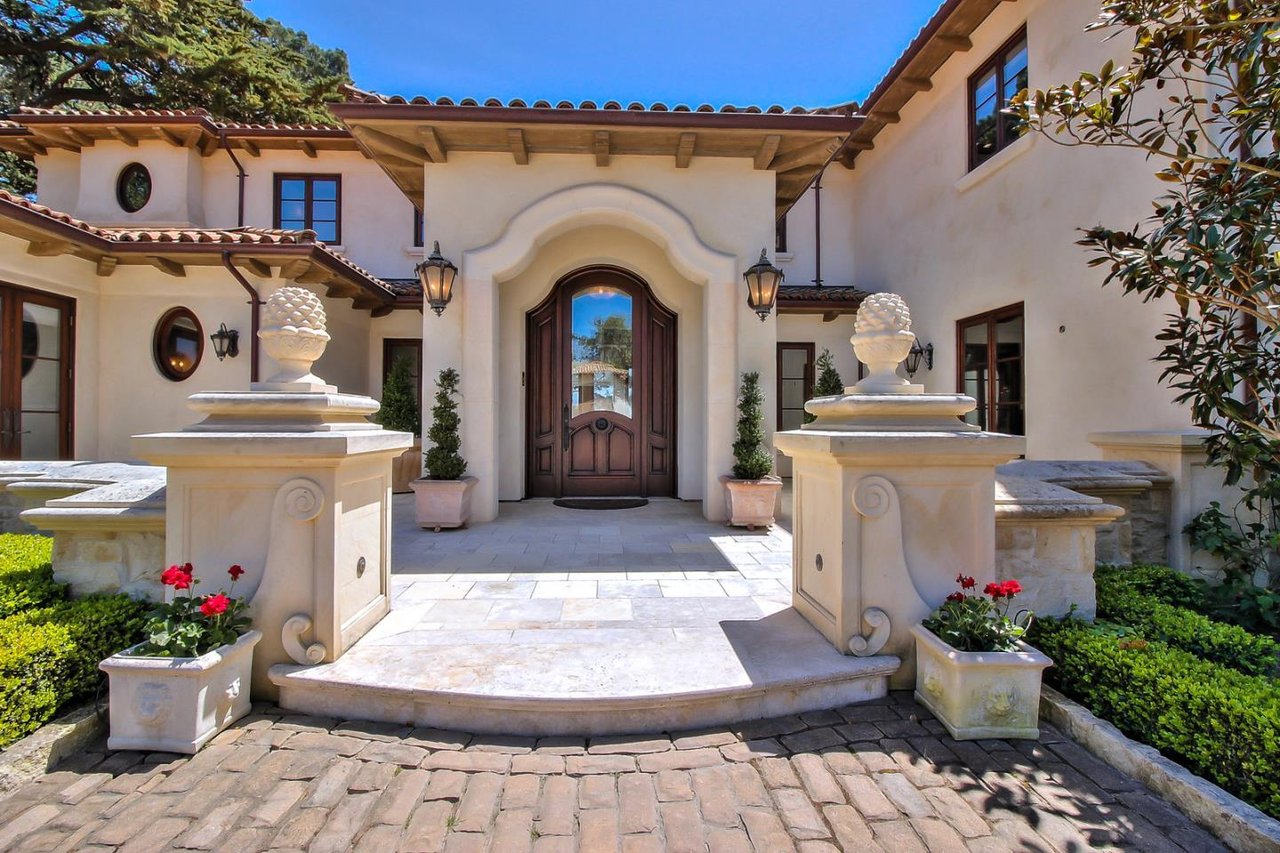 Mediterranean-style home entrance with an arched wood door and ornate stone planters.