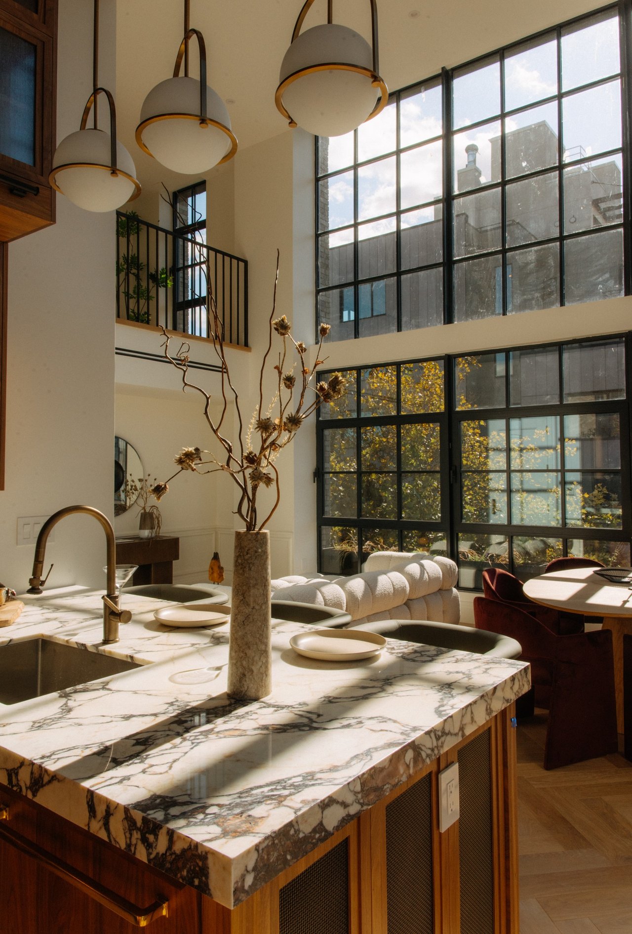 Double-height kitchen with a veined marble island, wood cabinetry, and tall black-framed windows.