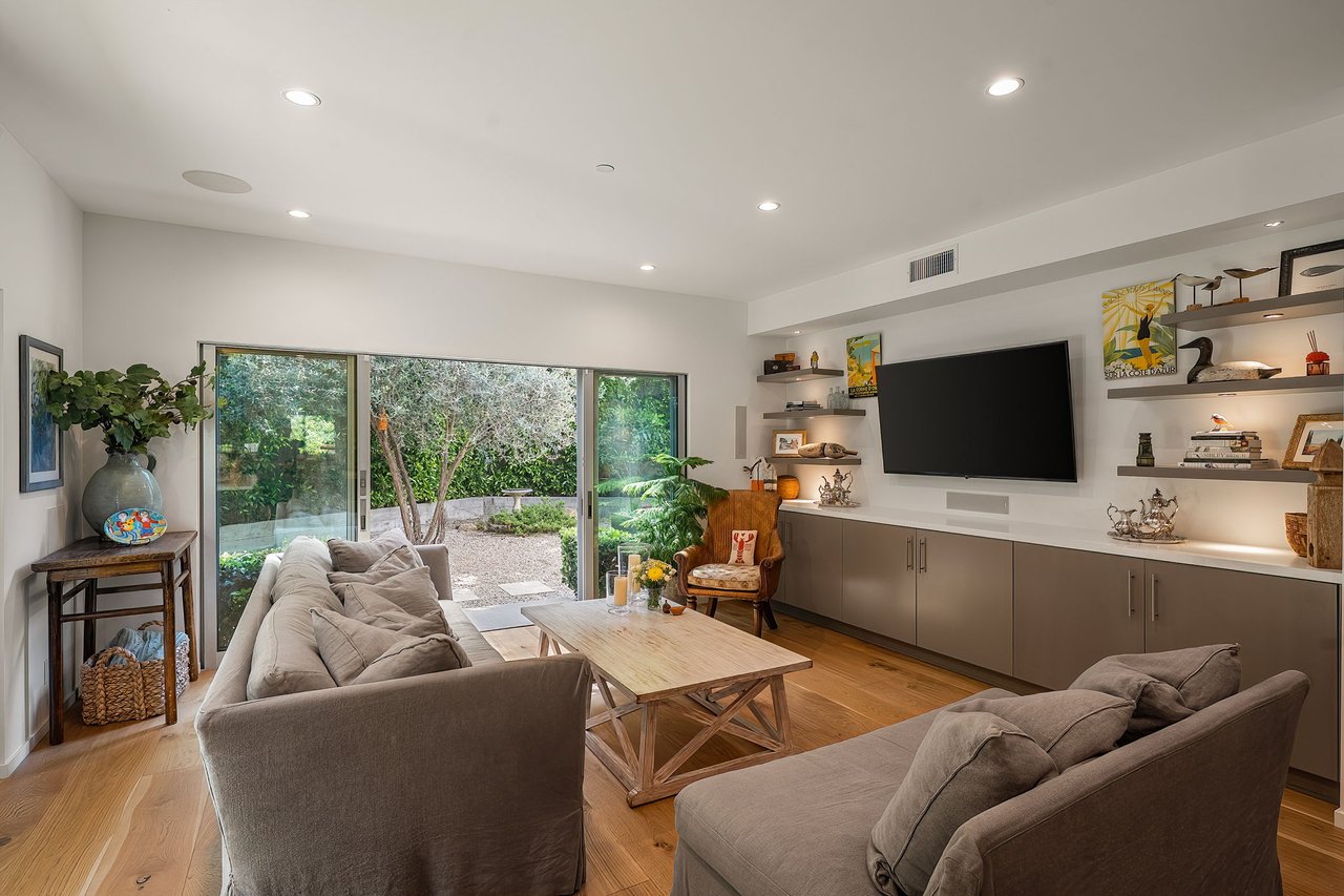 Living room with built-in shelves and sliding glass doors overlooking a leafy garden.