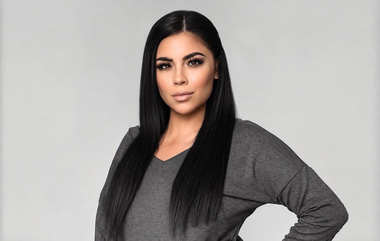 Mia Gomez in a charcoal gray top, with long dark hair and one hand on her hip.