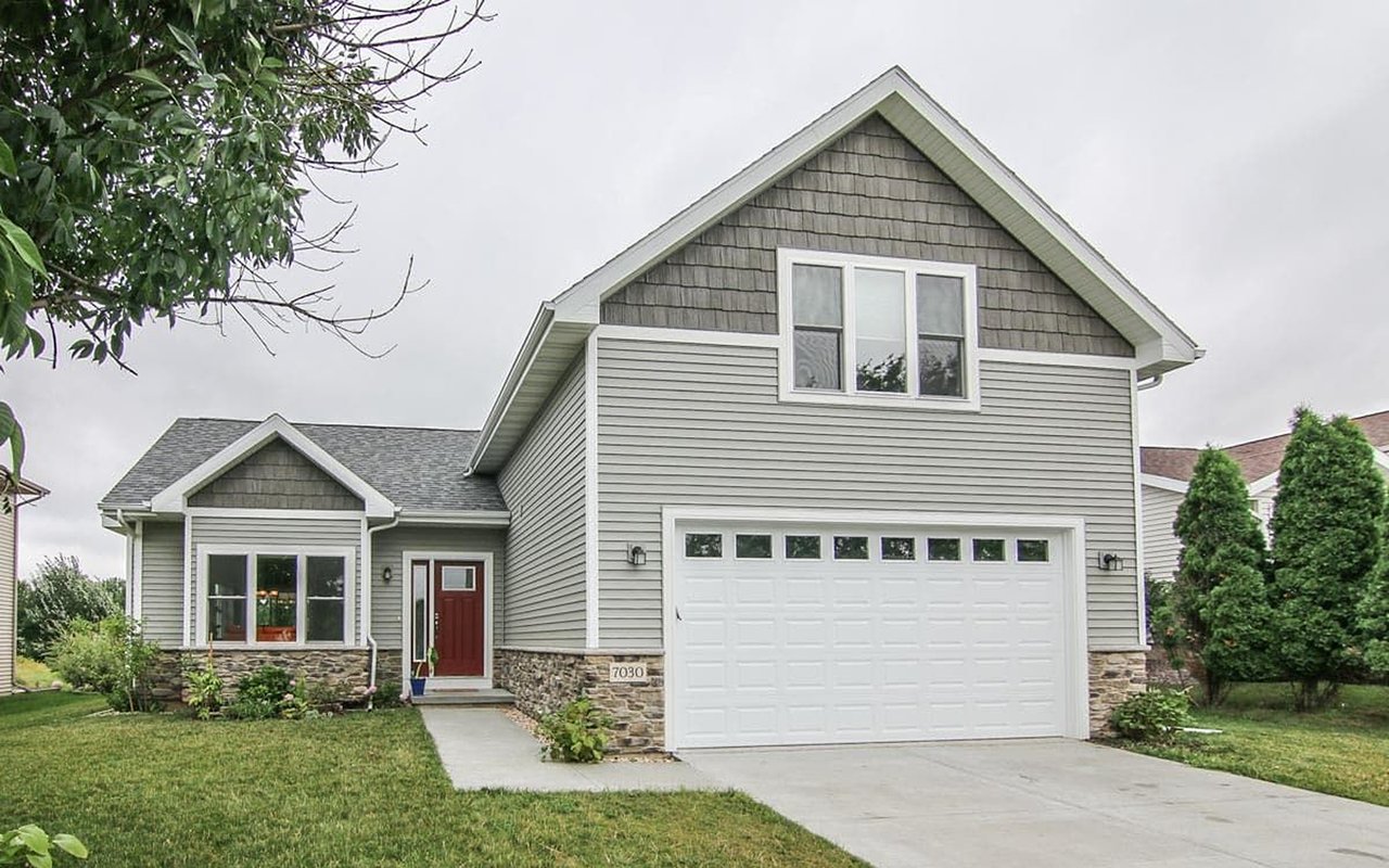 Gray two-story house with a steep gable, white garage door, red entry door, and stone accents.