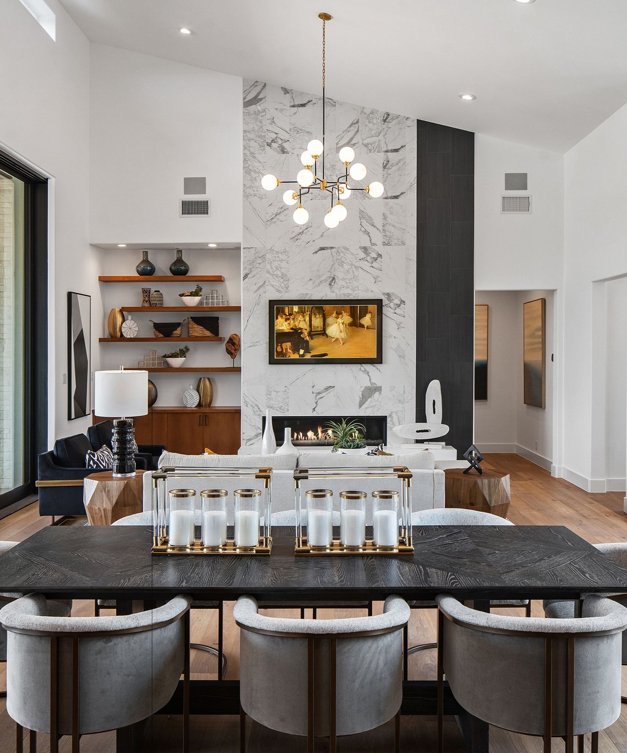 Modern living and dining room with a dramatic marble fireplace wall and sculptural chandelier.