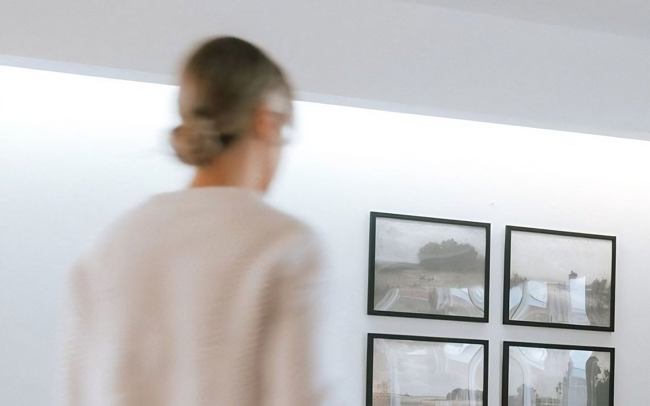 A woman examines four framed photographs on a wall inside a bright room.