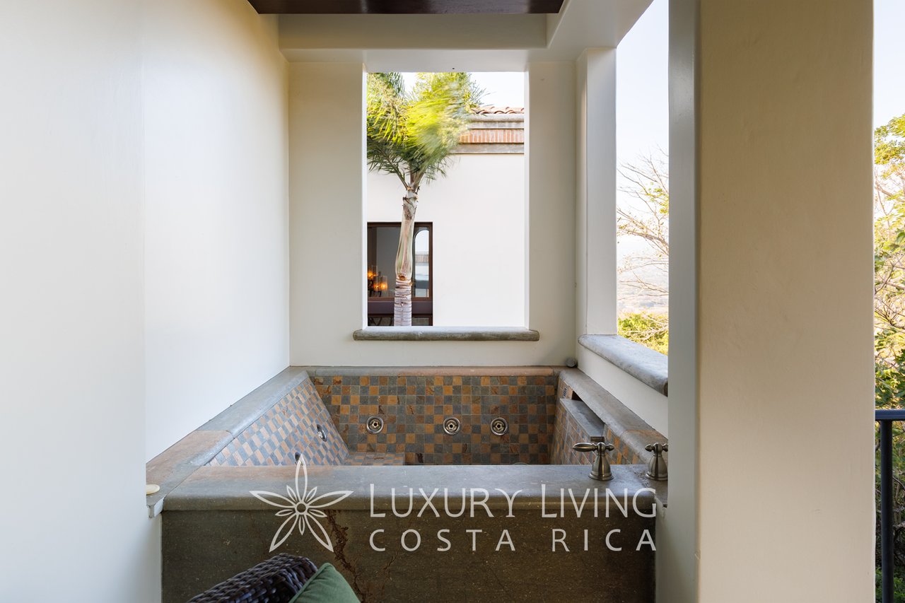 Covered outdoor soaking tub with patterned tile, stone ledges and brass faucets.