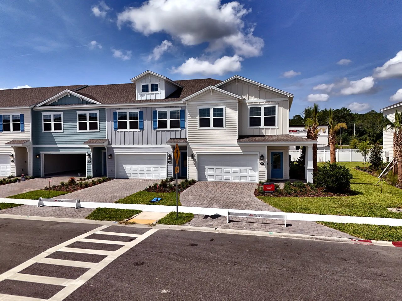 Attached two-story townhomes with garages, contrasting siding, and palm trees along the street.