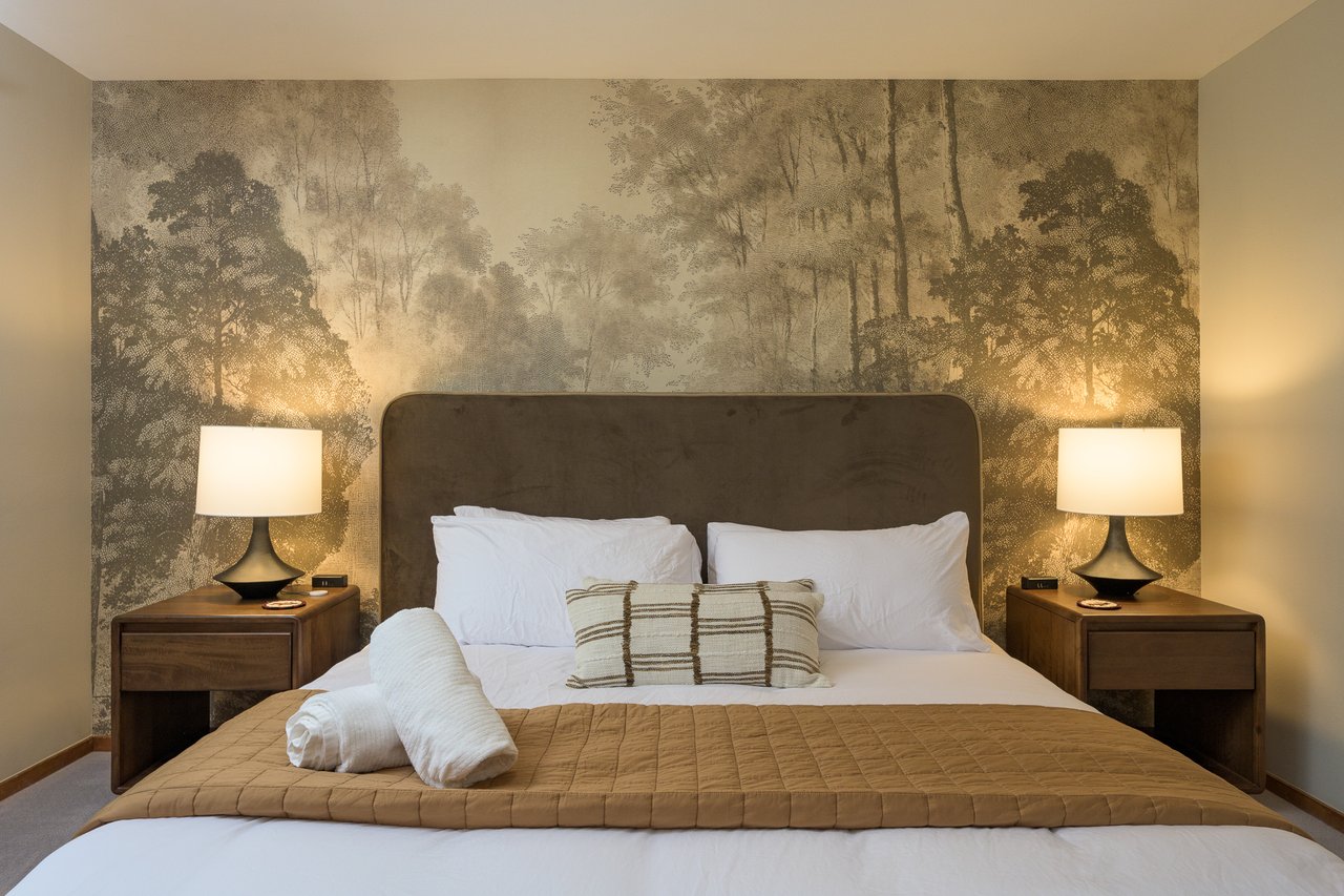 Bedroom with a woodland mural behind the bed and matching bedside lamps.