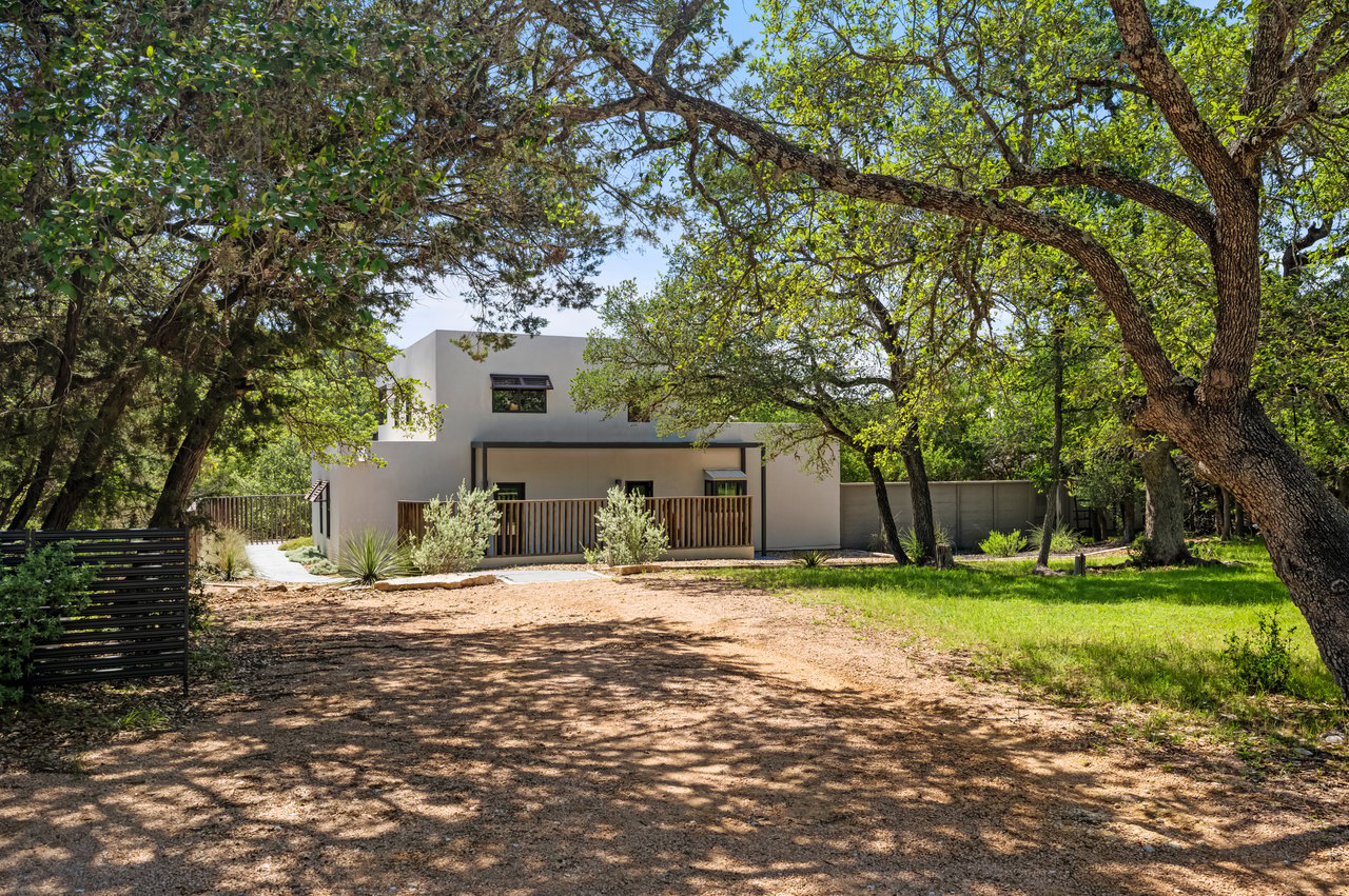 Modern two-story home beneath mature trees, with a covered porch and shaded driveway.