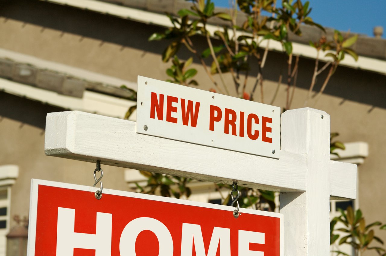 Real estate listing sign with “NEW PRICE” text in red, signaling a price reduction for a home that isn't selling fast.
