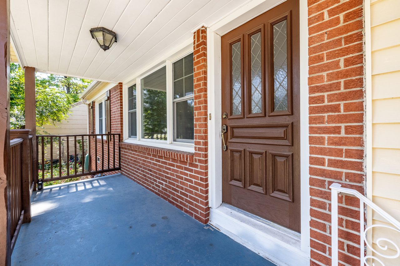 Covered brick front porch with a brown paneled door and dark railing.