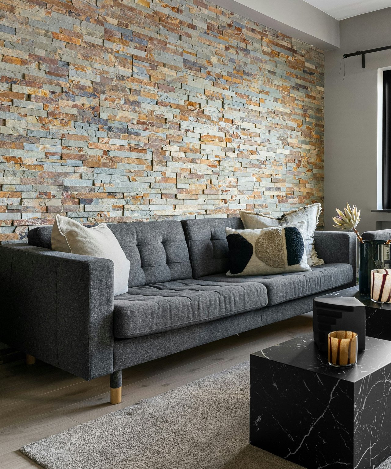 Living room with a charcoal sofa and colorful stacked-stone accent wall.