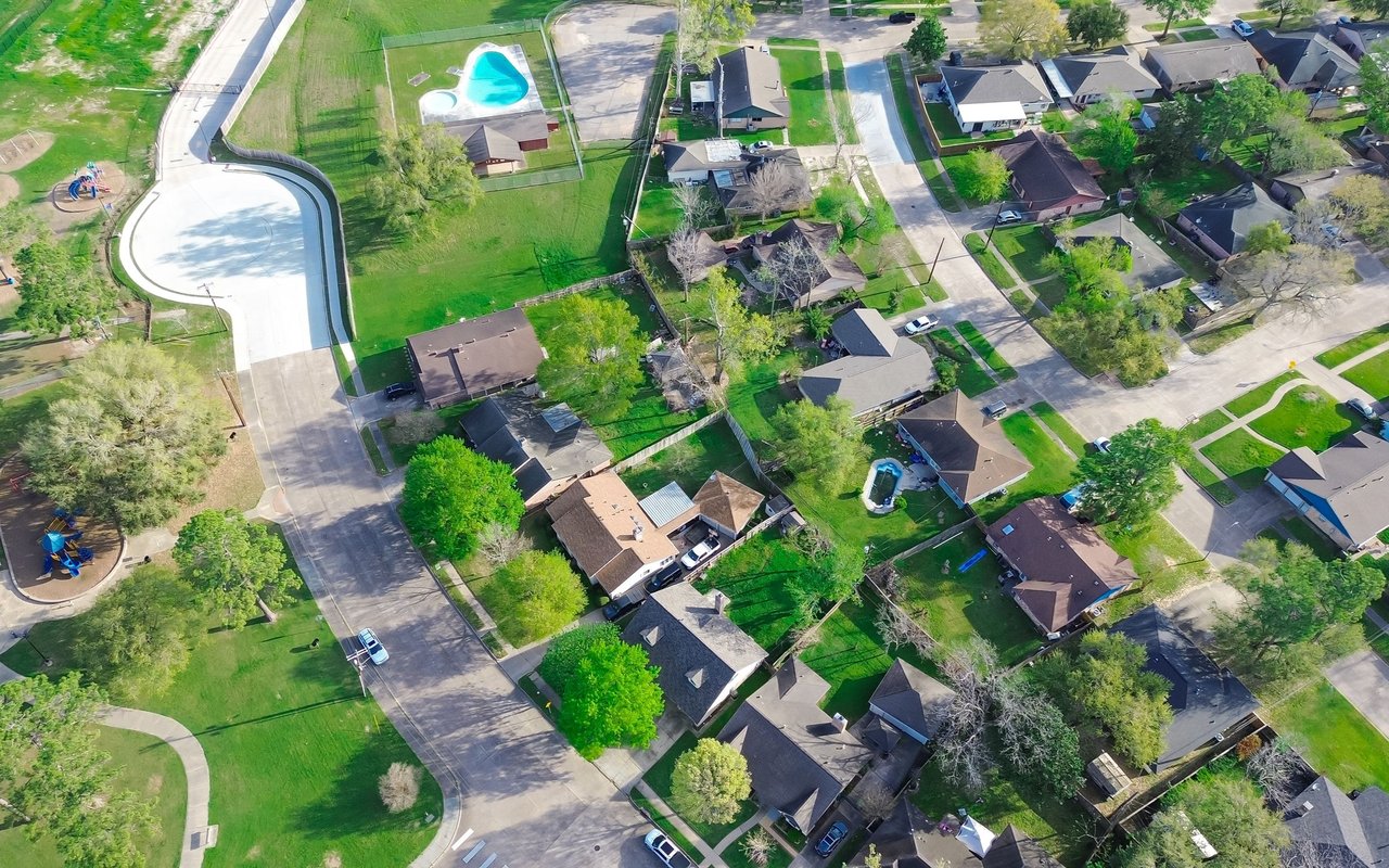 Aerial view of a suburban neighborhood with detached homes, tree-lined streets, and a community pool.
