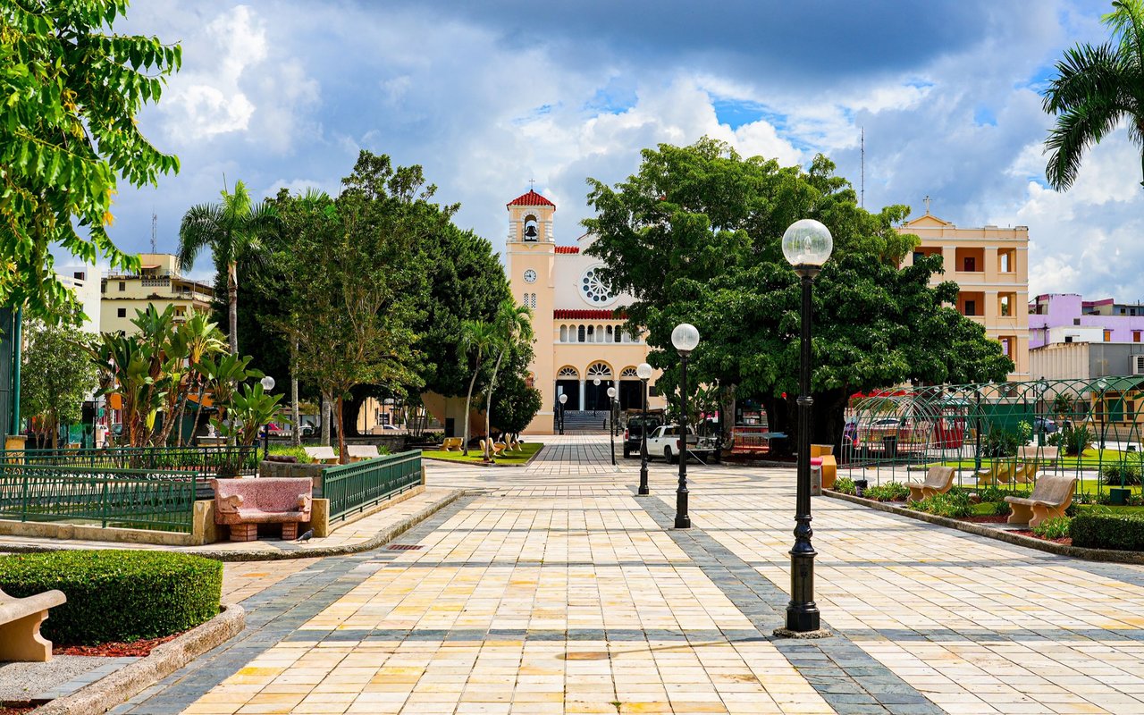 Town square in Caguas with a tiled plaza, garden benches, and a church bell tower.
