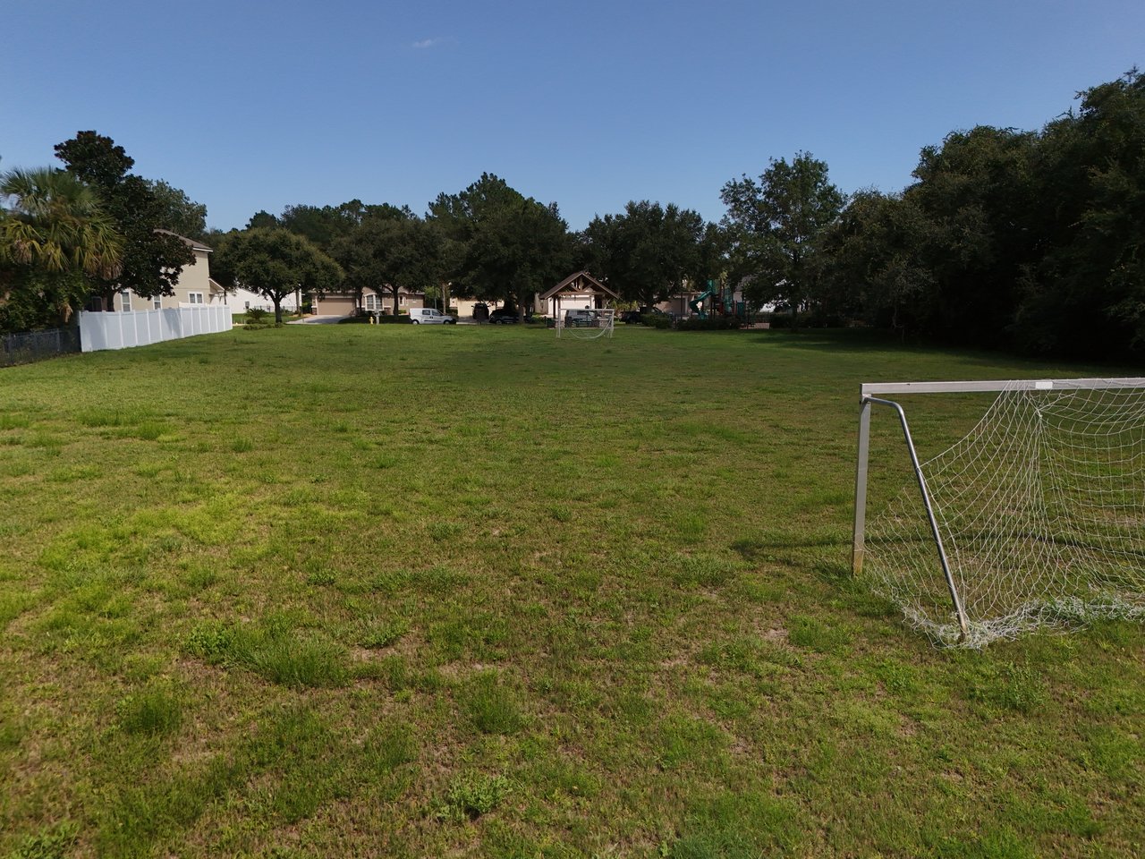 Neighborhood green space with soccer goals, a playground, and homes beyond the field.