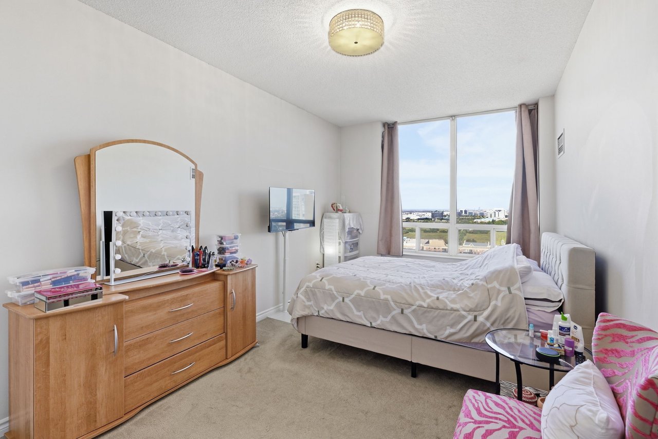 Furnished bedroom with a large window overlooking distant buildings and greenery.