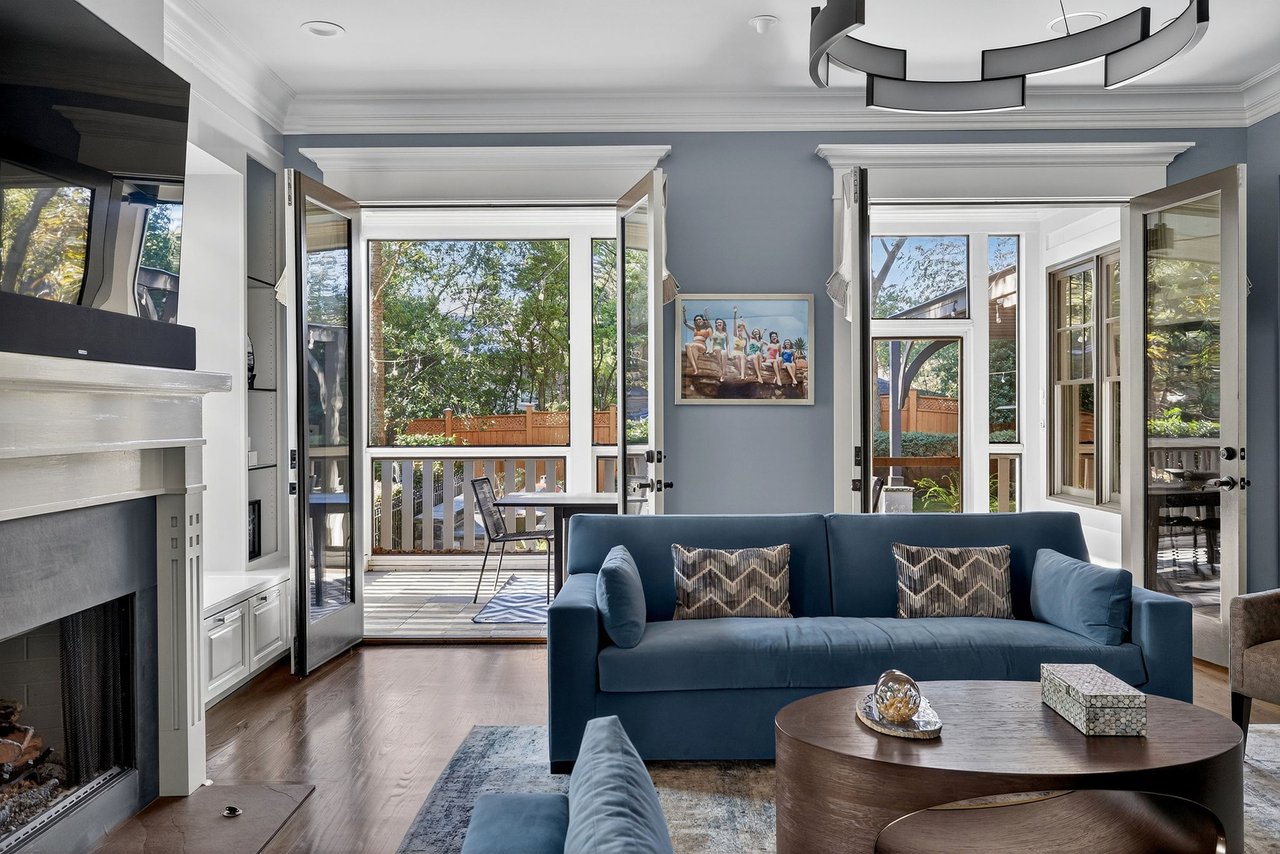 Living room with a blue sofa, fireplace, and open doors to a deck and leafy backyard.