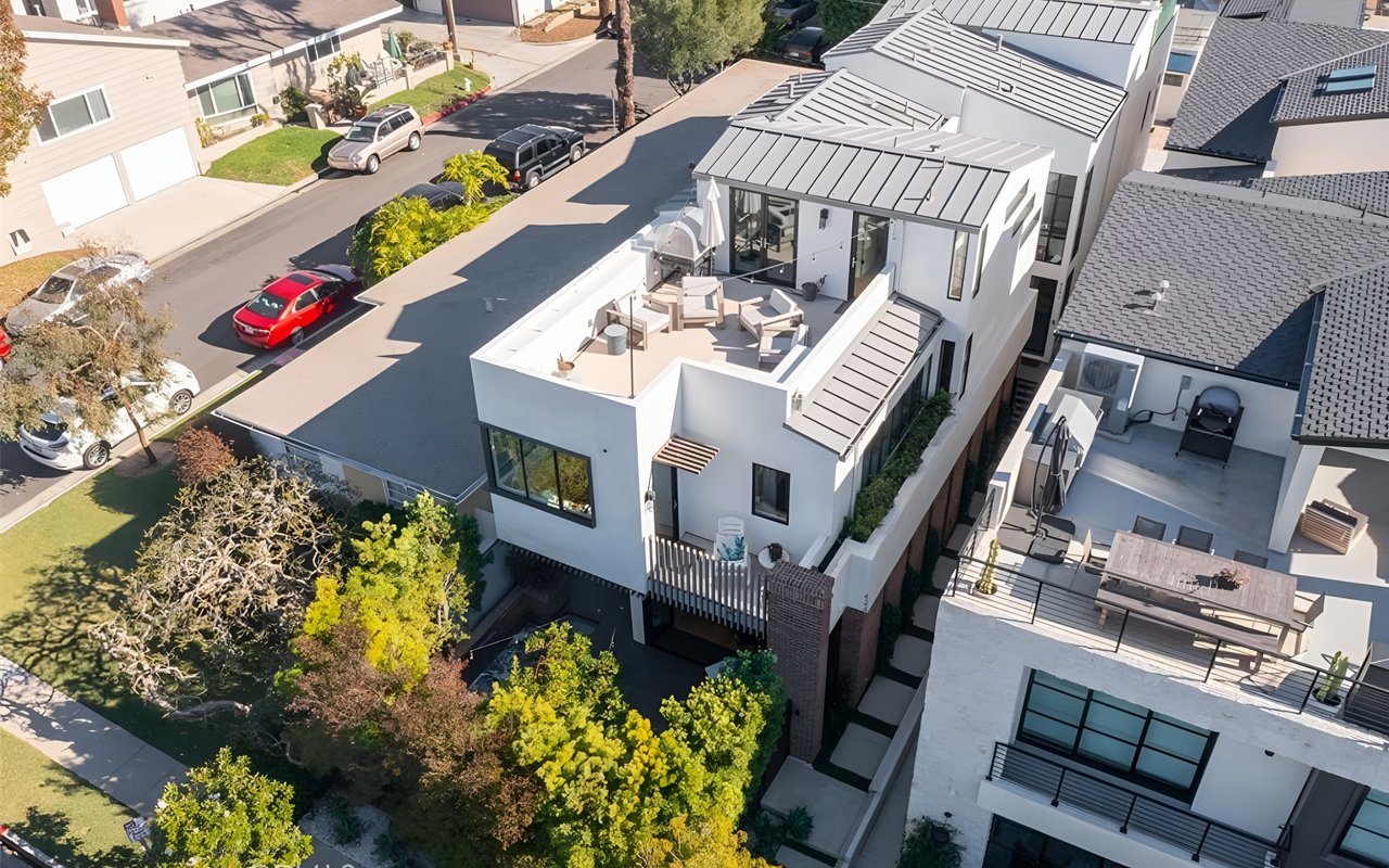 An aerial view of a modern white house with a rooftop patio, a front yard, and a two-car garage.