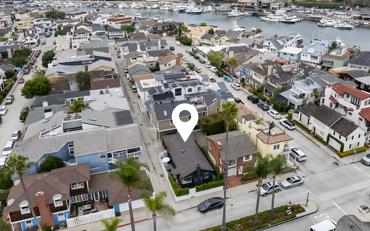  An aerial view of a coastal neighborhood with a large white pin marking a dark blue house near a marina filled with boats.