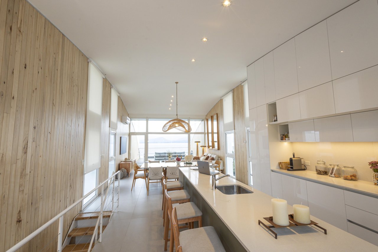 Open-plan apartment kitchen with a long island, wood-paneled walls, and water visible through the windows.