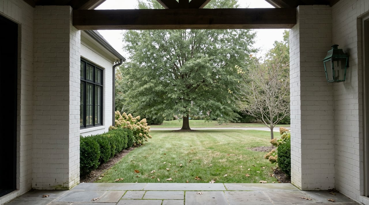 Painted-brick entry piers frame a bluestone threshold, lawn, and broad willow oak canopy.